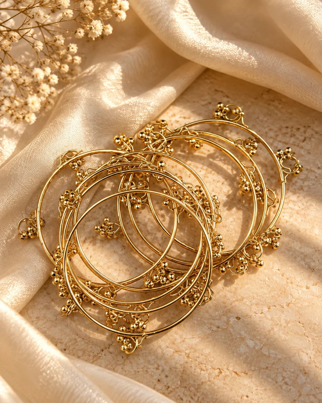 A stack of slim gold bangles with clustered gold bead drops on ivory silk and stone