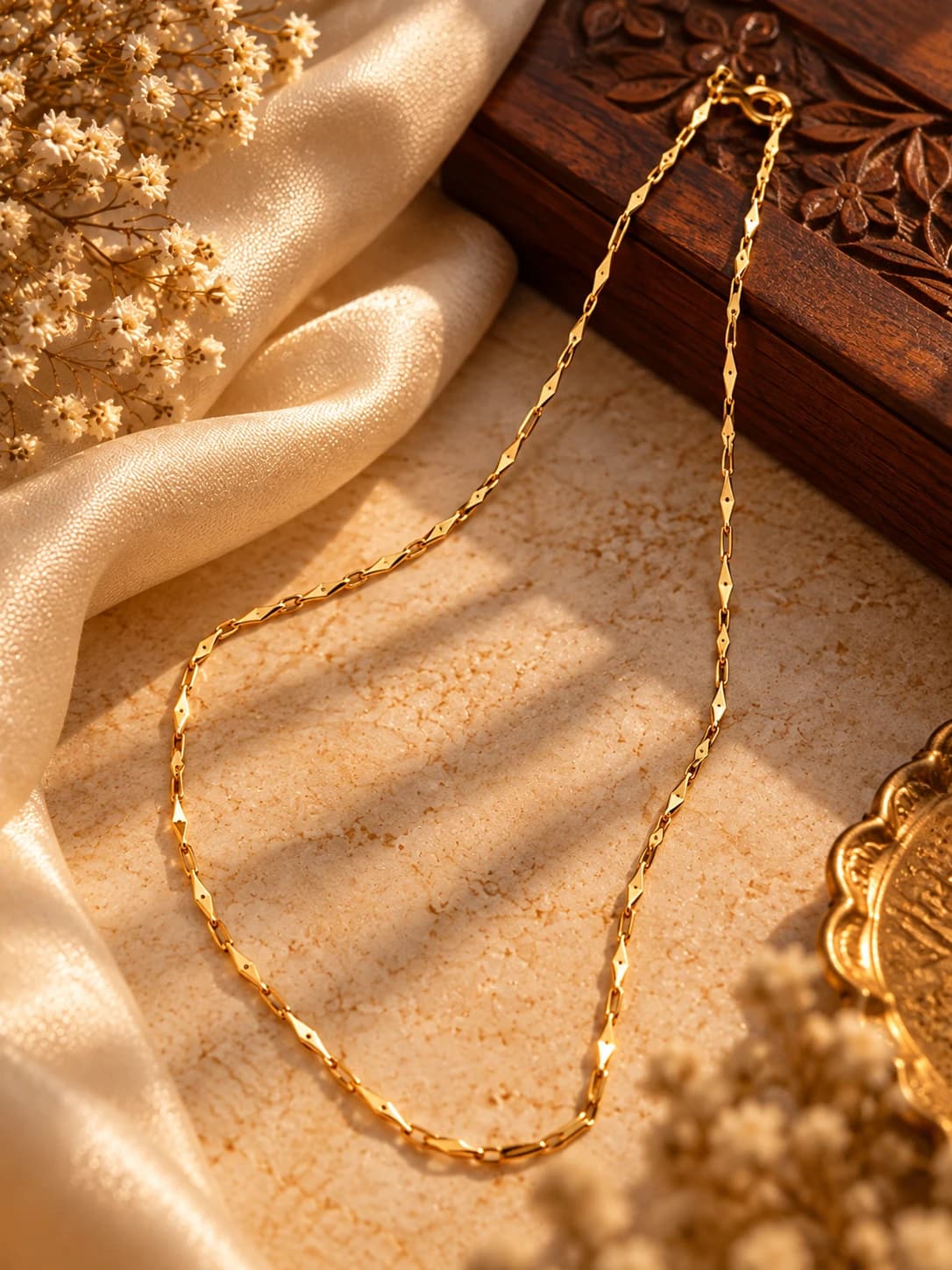 A delicate gold diamond-cut link chain laid on warm stone beside a carved wooden box